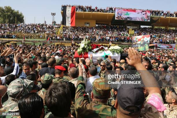Syrian mourners wave at the coffin of Brigadier General Issam Zahreddine at a stadium during his funeral in the southern city of Suwaida on October...