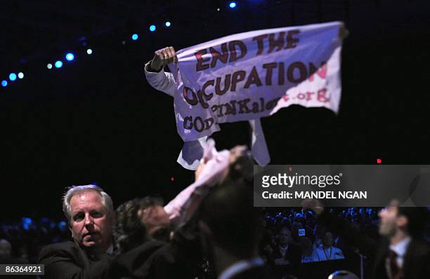 Protester unfurls a banner as Israeli President Shimon Peres addresses the American Israel Public Affairs Committee annual policy conference May 4,...