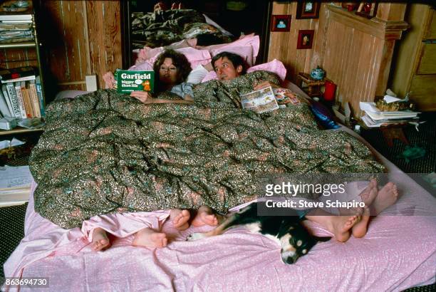 View of American married couple, actress Jane Fonda and politician and activist Tom Hayden , in bed, as the former reads aloud from 'Garfield Bigger...