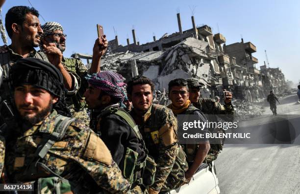 Kurdish fighters of the Syrian Democratic Forces ride in the back of a truck passing damaged buildings in Raqa on October 20 after a Kurdish-led...