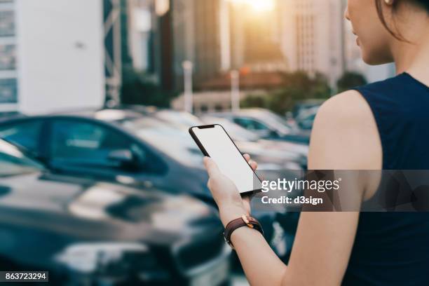 woman using smartphone while walking to her car in outdoor car park in city - chinese car home stock-fotos und bilder