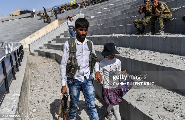 Fighter of the Syrian Democratic Forces walks with his daughter at the stadium in Raqa on October 20 as they celebrates the retakin gof the city from...