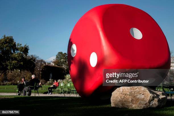 People sit next to the artwork 'The Misthrown Dice' by Gilles Barbier displayed at the Jardin des Tuilleries garden as part of the Paris...