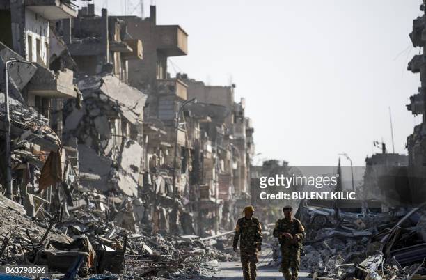 Fighters of the Syrian Democratic Forces walk down a street in Raqa past destroyed vehicles and heavily damaged buildings on October 20 after a...