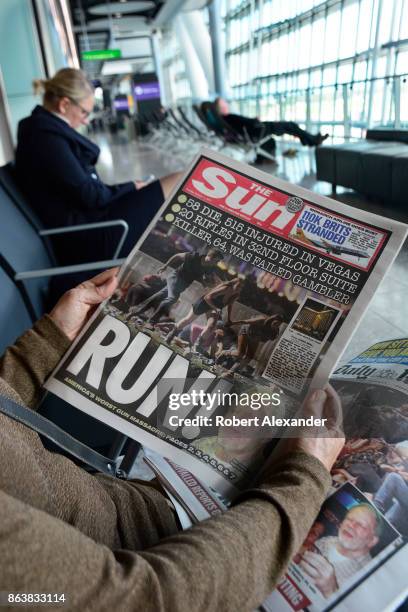 An airplane passenger waiting to board a flight at Heathrow International Airport in London, England, reads copies of two English tabloid newspapers,...