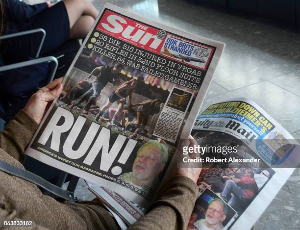 An airplane passenger waiting to board a flight at Heathrow International Airport in London, England, reads copies of two English tabloid newspapers,...