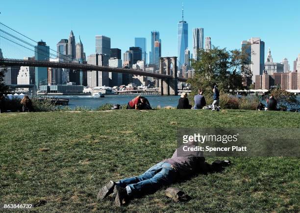 People relax along a promenade in Brooklyn on an unseasonably warm day on October 20, 2017 in New York City. Temperatures across New England are...