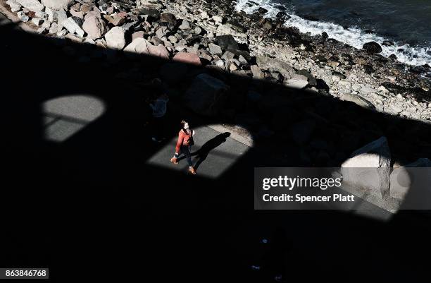 People walk along a promenade in Brooklyn on an unseasonably warm day on October 20, 2017 in New York City. Temperatures across New England are...