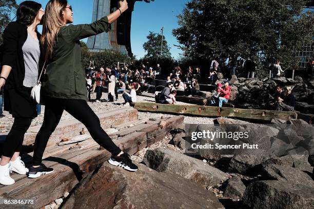 People relax along a promenade in Brooklyn on an unseasonably warm day on October 20, 2017 in New York City. Temperatures across New England are...