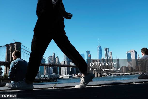 People relax along a promenade in Brooklyn on an unseasonably warm day on October 20, 2017 in New York City. Temperatures across New England are...