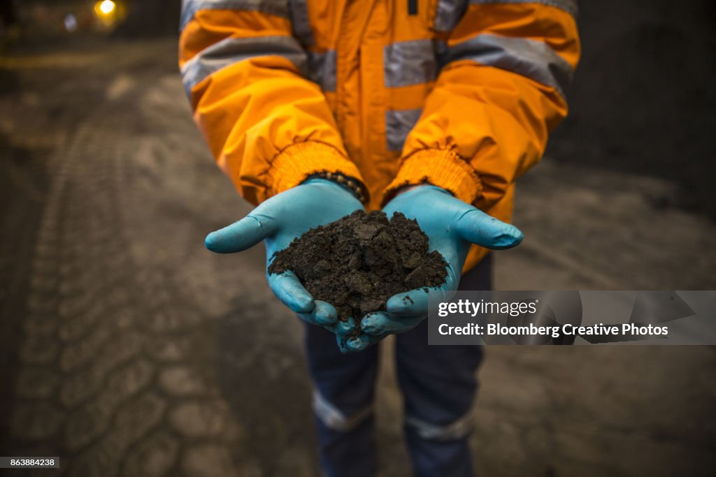 An employee holds a pile of copper concentrate at a refinery and smelter