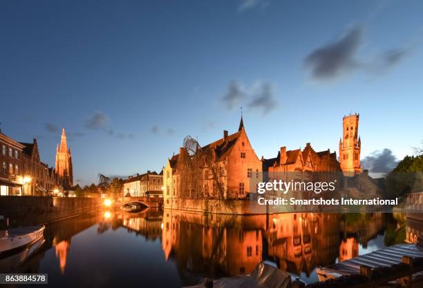 wide angle, full length image of romantic rozenhoedkaai canal, belfry of bruges and church of our lady spire illuminated at late dusk in bruges, flanders, belgium - bruges night stock pictures, royalty-free photos & images