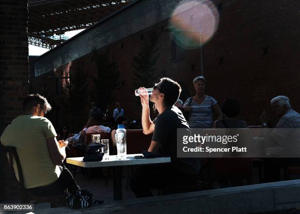 People eat lunch along a promenade in Brooklyn on an unseasonably warm day on October 20, 2017 in New York City. Temperatures across New England are...
