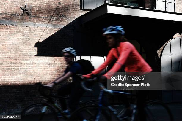 People bike along a promenade in Brooklyn on an unseasonably warm day on October 20, 2017 in New York City. Temperatures across New England are...