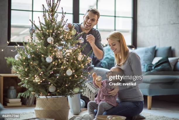 happy family decorating tree - decorating christmas tree stock pictures, royalty-free photos & images