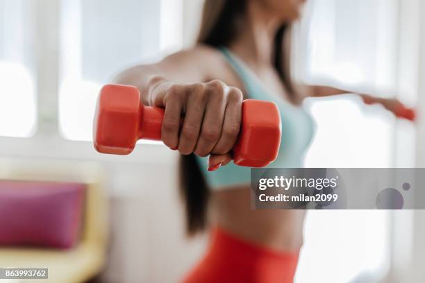 young woman exercising with her weights in the living room - woman arm around stock pictures, royalty-free photos & images