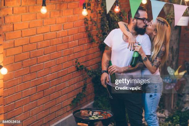 tätowierte paare, die spaß am grillen im hinterhof - couple grilling stock-fotos und bilder