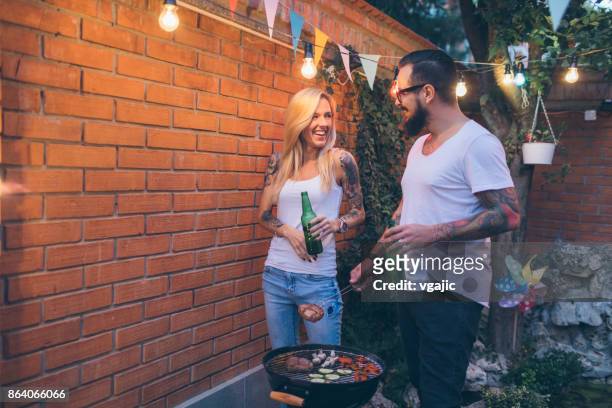 tattooed couple having fun at barbecue in backyard - couple grilling stock pictures, royalty-free photos & images