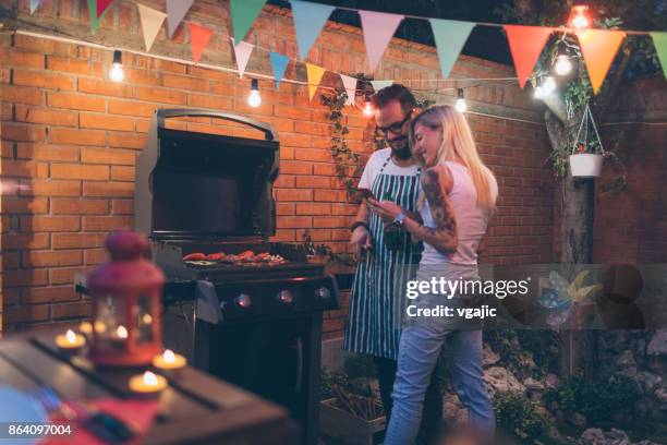 tattooed couple having fun at barbecue in backyard - couple grilling stock pictures, royalty-free photos & images