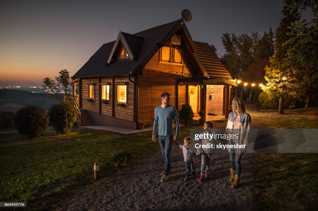 Happy family holding hands and walking by their chalet in the evening.