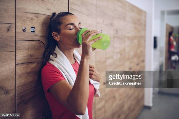 mujer agotada de beber agua en los vestuarios después de entrenamiento deportivo. - vestuario entre bastidores fotografías e imágenes de stock