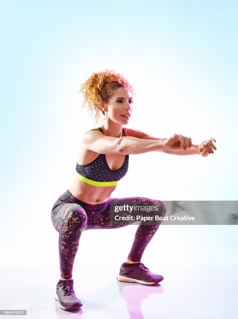 Woman with curly red hair smiling while doing air lunge
