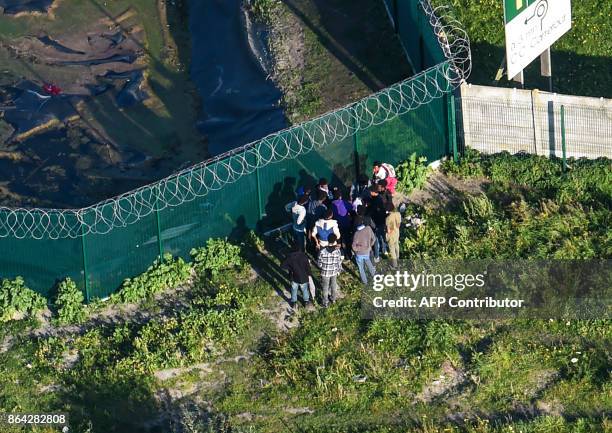 This aerial view shows migrants gather on October 14, 2017 by a petrol station's fence, near the former "Jungle" migrant camp that was evacuated 12...