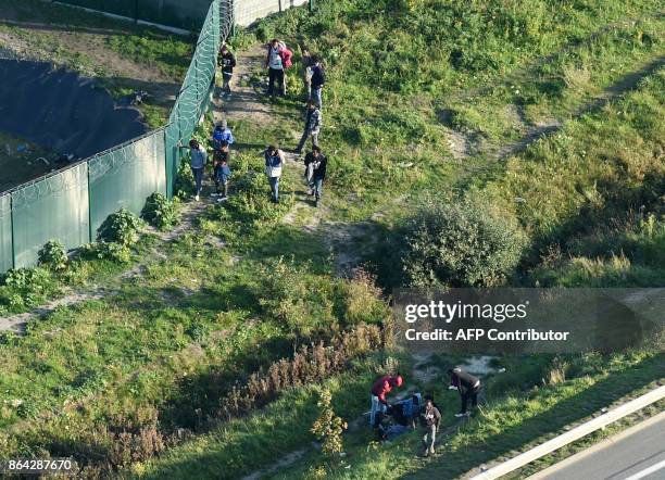 This aerial view shows migrants gather on October 14, 2017 by a petrol station's fence along the A216 highway, near the former "Jungle" migrant camp...