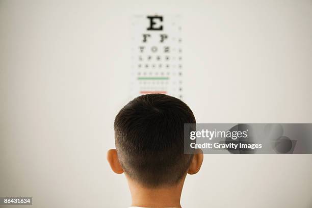 young boy looking at wall eye chart - optical equipment stock pictures, royalty-free photos & images