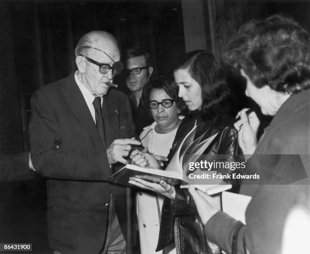 American film director John Ford signs autographs for a group of fans, circa 1965.