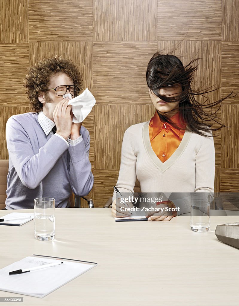 Man sneezing on woman in office environment