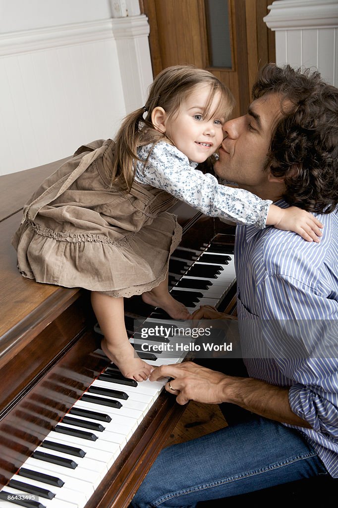 Father kissing young daughter while playing piano