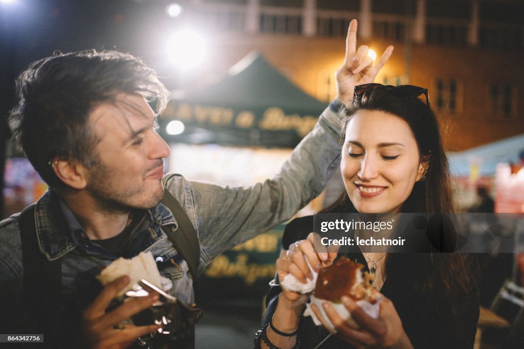 Two young people having fun eating street food in London at night