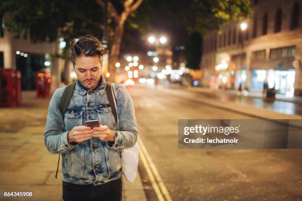jongeman texting terwijl het lopen in de straten van londen 's nachts - city of london stockfoto's en -beelden