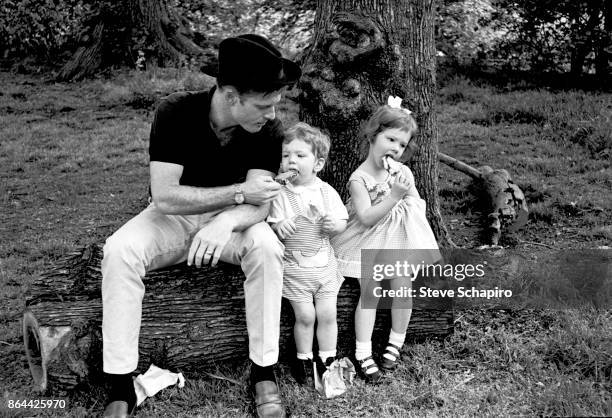 Portrait of American actor Robert Redford, in a black hat, and his children, David and Shauna, as they all sit on a log and eat ice cream in Central...