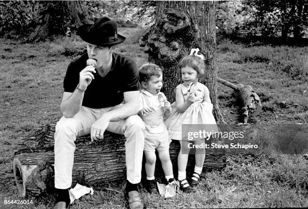 Portrait of American actor Robert Redford, in a black hat, and his children, David and Shauna, as they all sit on a log and eat ice cream in Central...