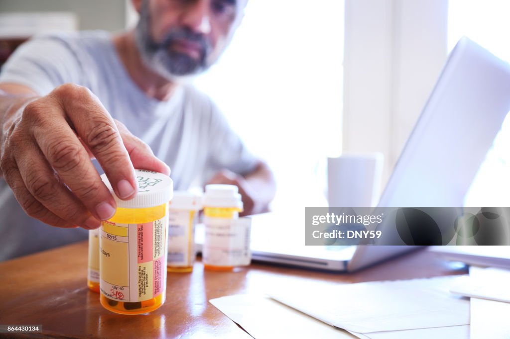 Hispanic Man Sitting At Dining Room Table Reaches For His Prescription Medications