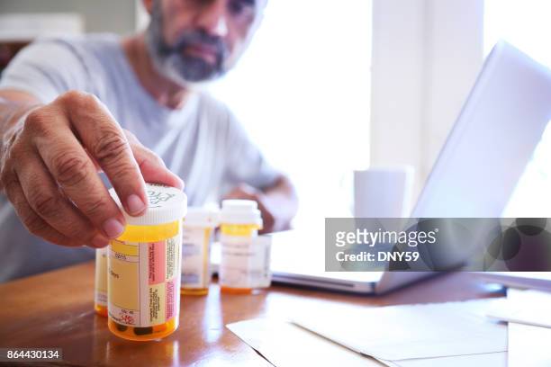 hispanic man sitting at dining room table reaches for his prescription medications - prescription medicine stock pictures, royalty-free photos & images
