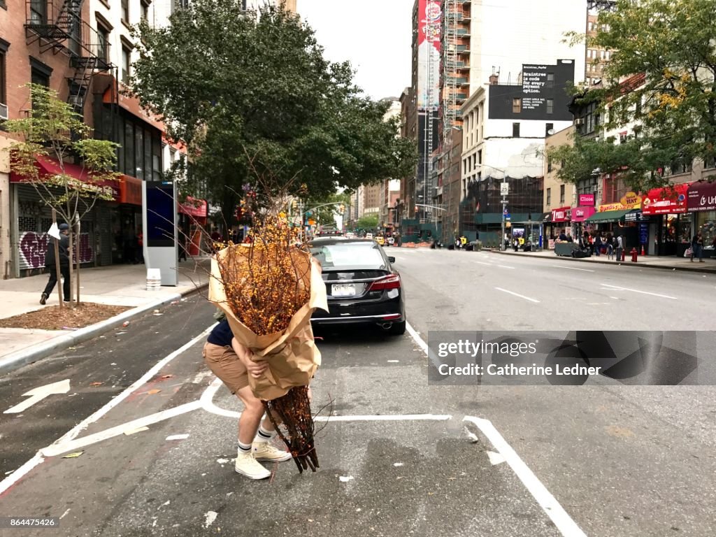 Man picking up large dried plant wrapped in brown paper on the street