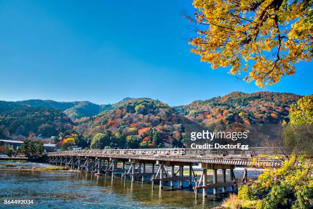 togetsukyo bridge across hozugawa river and yellow ginko tree with colourful maple tree on the mountain background, arashiyama, kyoto in autumn - arashiyama imagens e fotografias de stock