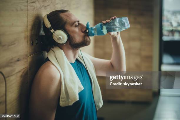 young sportsman with headphones drinking fresh water at gym's locker room. - locker room drinking water stock pictures, royalty-free photos & images