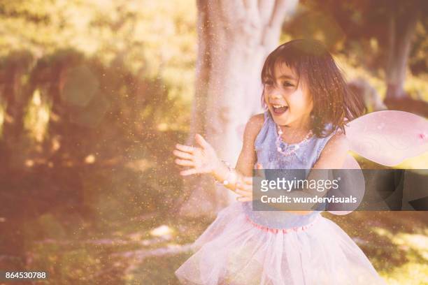 smiling little girl playing dress-up and blowing glitter in park - the fairy queen stock pictures, royalty-free photos & images