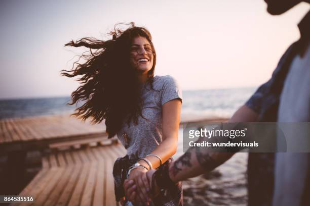 tenue de couple jeune hipster ludique les mains sur la jetée au coucher du soleil - ponton bois photos et images de collection