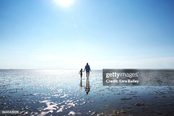 mother and son walking along the beach at low tide. - sea clear sky stock pictures, royalty-free photos & images