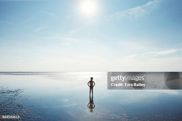 Young boy standing in shallow water at low tide.