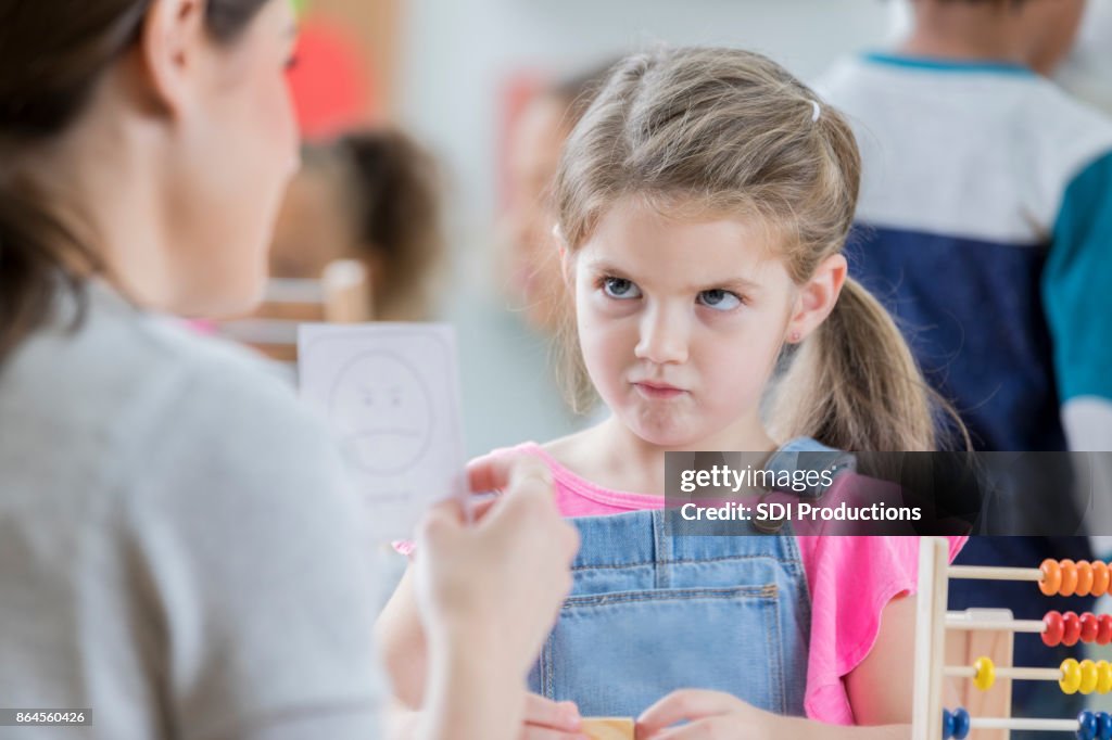 Young schoolgirl mimics face on emotion flash card