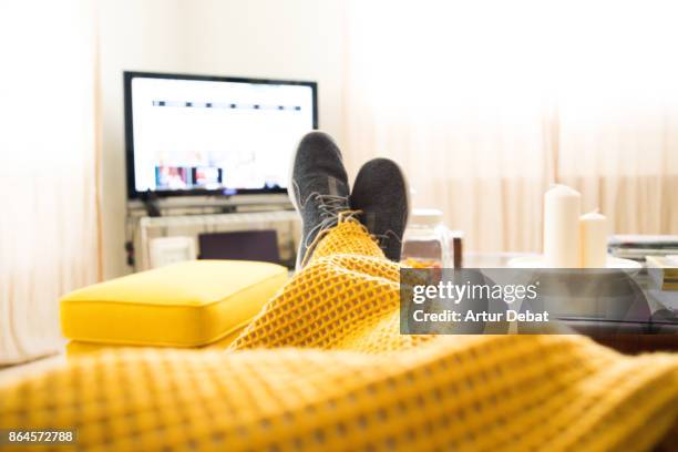 guy relaxing at home from personal perspective laying in sofa in autumn day covering with blanket while watching television. - zapatos-amarillos fotografías e imágenes de stock
