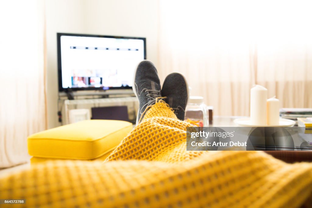 Guy relaxing at home from personal perspective laying in sofa in autumn day covering with blanket while watching television.