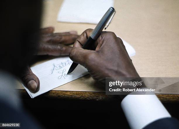 Jazz musician and singer Louis Armstrong signs an autograph in his makeshift dressing room prior to performing with his band in a high school...