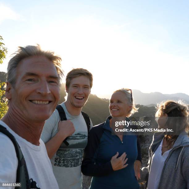 family of hikers pause on hillcrest at sunrise, looking at camera - family trip in laws stock pictures, royalty-free photos & images